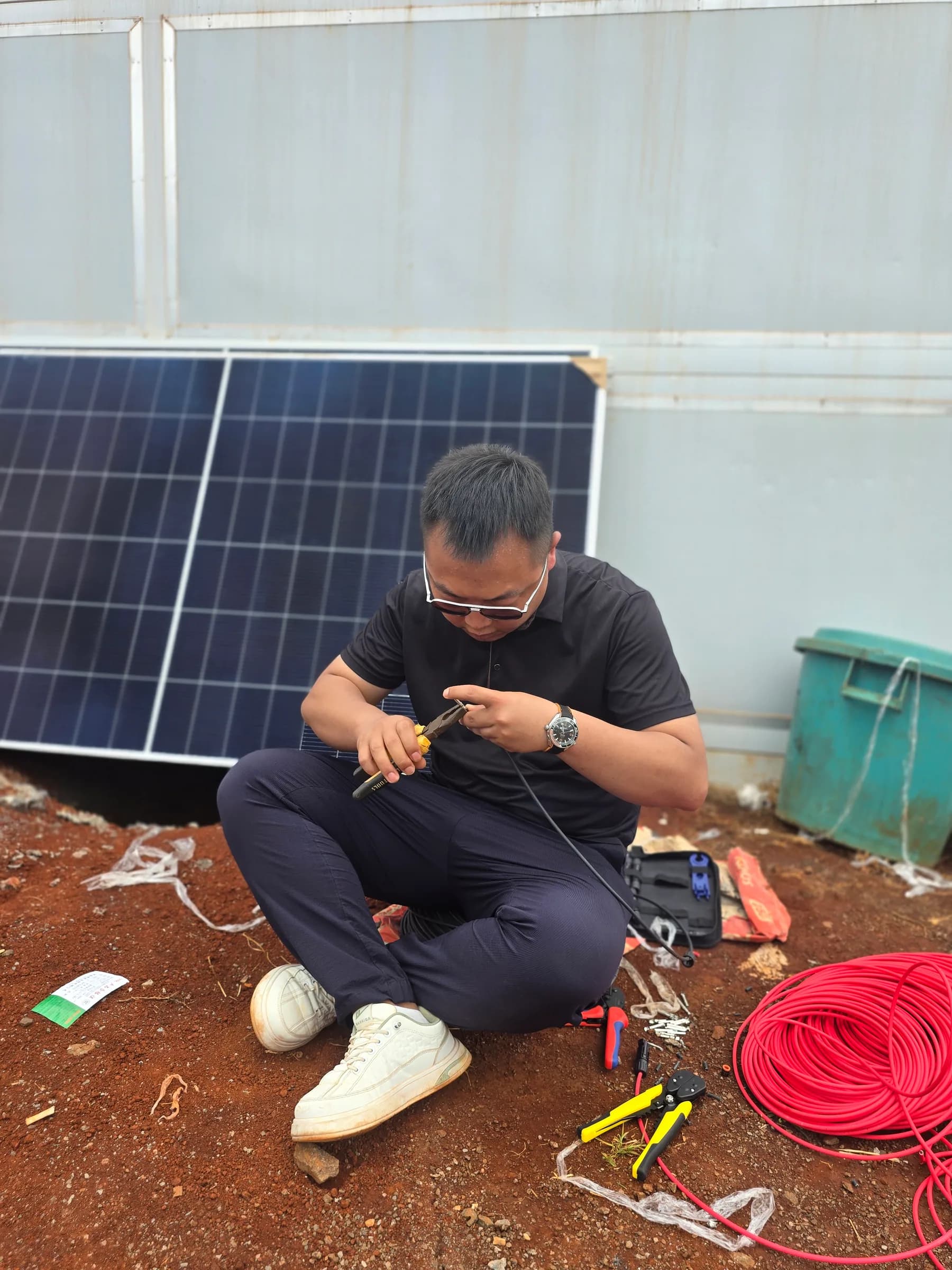 Solar technician preparing red DC cable beside photovoltaic modules.